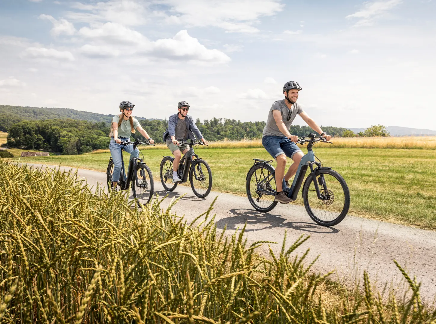 Eine Frau und zwei Männer fahren mit ihren Focus Planet2 EBike City Bikes auf einem Feldweg entlang