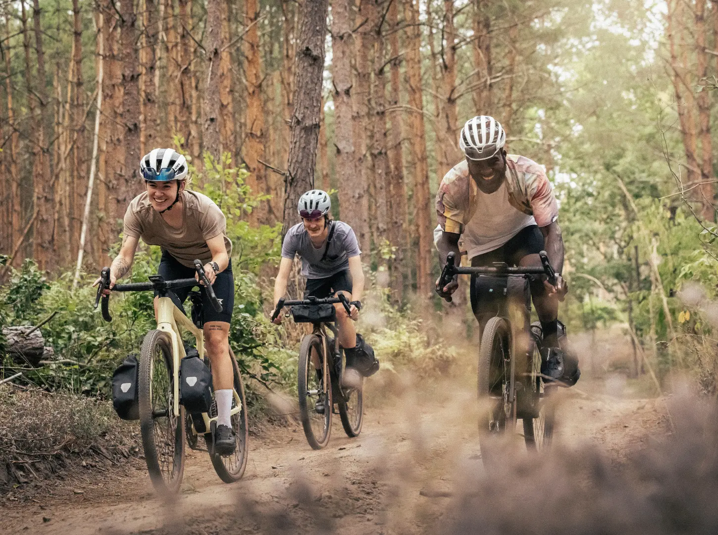 Eine Frau und zwei Männer fahren mit ihren Focus Atlas Gravelbikes durch den Wald